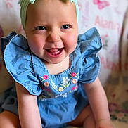 Alani is registered to the contest to win money with this photo: baby, child, smiling, headband, bow, blue_dress, sitting, happy, infant, cute, portrait, indoors, blanket, butterfly_pattern, footwear, colorful_shoes, skin, face, person, young_child