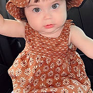 Giselle joined the competition — help win amazing prizes! baby, child, car_seat, hat, dress, patterned_clothing, cute, infant, face, eyes, chubby_cheeks, sitting, indoors, portrait, person, headwear, clothing, seat, young_child, adorable