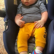 Jaxson is registered to the contest to win money with this photo: baby, infant, car_seat, child, toddler, yellow_pants, grey_shirt, colorful_sandals, socks, floor, tile_floor, indoor, footwear, seated, cute, small_hands, young_child, casual_clothing, resting, portrait