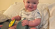 Sawyer is registered to the contest to win money with this photo: baby, smiling, toys, pillow, bed, child, indoor, clothing, happy, face, person, infant, cute, sitting, playful, cushion, home, blanket, foot, light