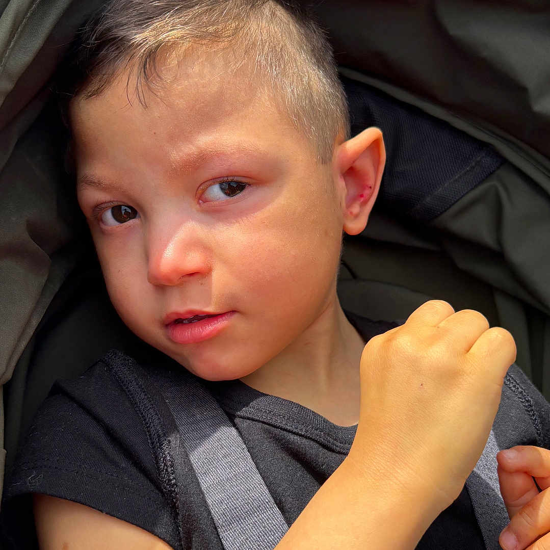 Lennox joined the competition — help win amazing prizes! child, boy, stroller, harness, portrait, closeup, serious, face, arm, black_shirt, short_hair, daylight, outdoor, seatbelt, baby, skin, expression, person, young, sitting