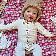 Léonie participe au concours pour gagner de l'argent avec cette photo : baby, infant, smile, hat, bear_ears, knitwear, buttoned_outfit, lying_down, blanket, checkered_pattern, red, white, cream_color, happy, cute, child, portrait, indoors, cozy, soft_texture