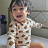 toddler, child, bed, onesie, bear_pattern, smiling, happy, indoor, white_sheets, window_light, metal_bed_frame, sitting, cute, young_child, hair, sock, room, furniture, baby, portrait