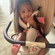 Maya joined the competition — help win amazing prizes! baby, child, stroller, seatbelt, foot, hand, smile, happy, indoor, clothing, pigtails, face, person, infant, cute, baby_girl, playful, human, transport, comfort