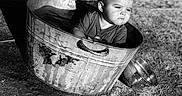 Theodore is registered to the contest to win money with this photo: toddler, child, metal_tub, water, outdoor, black_and_white, car_tire, sand, small_bowl, curious, expression, rustic, sunlight, shadow, clothing, portrait, sitting, play, young_child, daylight