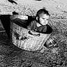 black_and_white, car_tire, child, clothing, curious, daylight, expression, metal_tub, outdoor, play, portrait, rustic, sand, shadow, sitting, small_bowl, sunlight, toddler, water, young_child