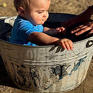 Theodore joined the competition — help win amazing prizes! baby, child, toddler, blue_shirt, metal_tub, water, hands, outdoor, sunlight, sand, play, splash, skin, face, expression, summer, fun, curious, person, closeup
