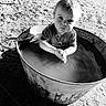 toddler, child, water, metal_tub, outdoor, sand, dog, black_and_white, portrait, curious, clothing, hands, face, animal, pet, sunlight, shadow, play, young_child, expression