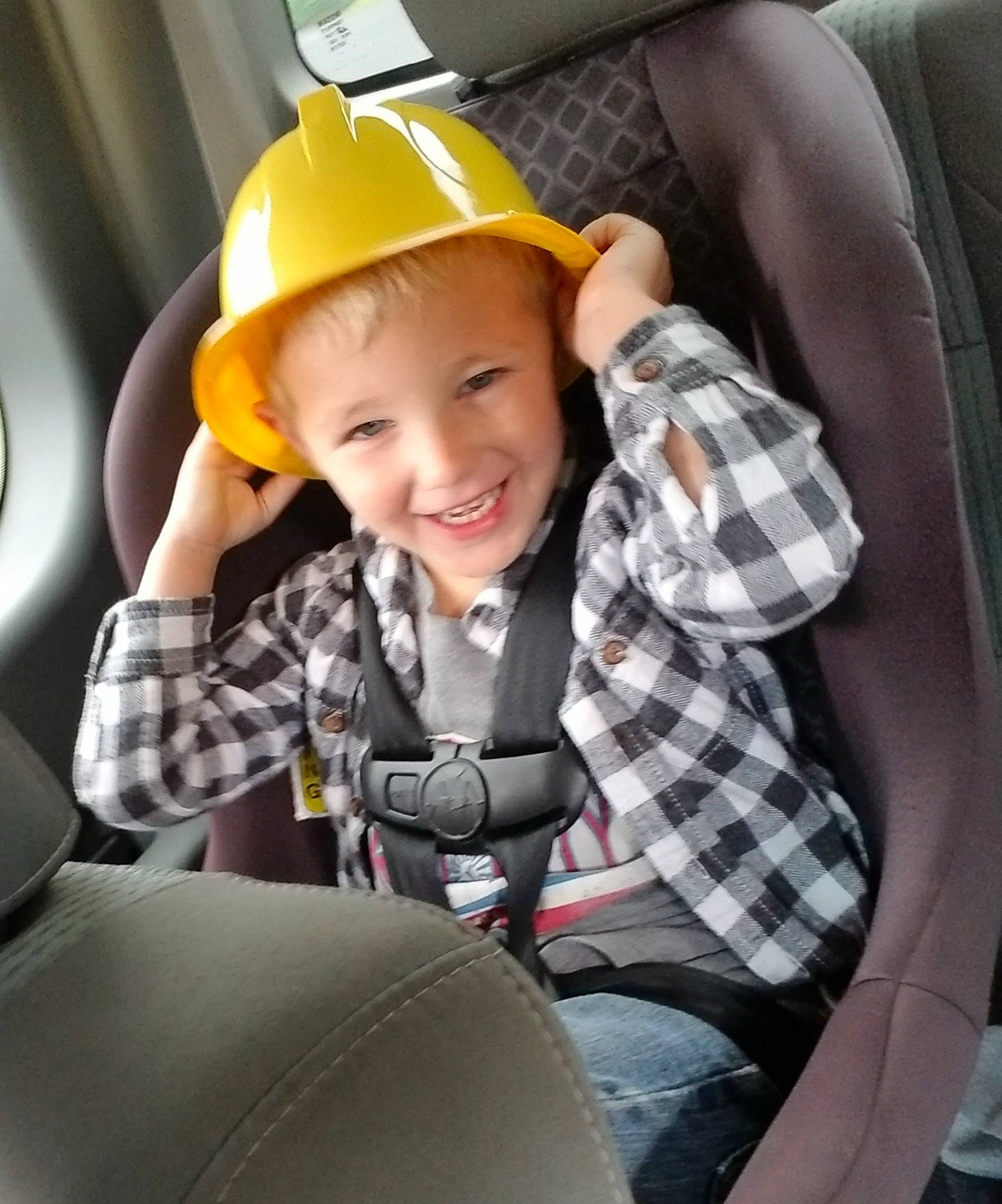 Sebastian is registered to the contest to win money with this photo: auto_part, car_seat, child, hard_hat, hat, headgear, headwear, helmet, joy, person, personal_protective_equipment, seat_belt, smile, toddler