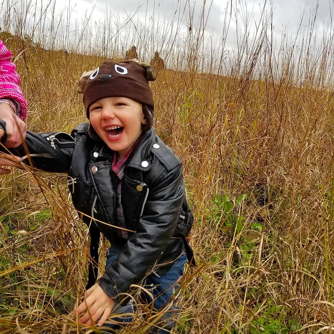 Sebastian is registered to the contest to win money with this photo: child, grass, grass_family, grassland, happy, headwear, jacket, joy, meadow, natural_landscape, outerwear, person, photography, plant, play, prairie, recreation, toddler, tree, wilderness