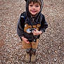 child, smiling, hoodie, bear_ears, backpack, boots, gravel, outdoor, cute, happy, young_child, casual_clothing, standing, portrait, nature, brown, gray, playful, kid, fall