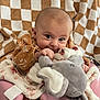 Khaleesi is registered to the contest to win money with this photo: baby, infant, plush_toy, elephant_toy, blanket, checkered_pattern, brown_clothing, pink_seat, cute, child, smiling, indoors, portrait, young_child, soft_texture, cozy, happy, face, hand, sitting