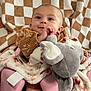 Khaleesi is registered to the contest to win money with this photo: baby, infant, blanket, plush_toy, elephant_toy, pink_seat, checkered_background, clothing, smiling, cute, child, face, portrait, indoor, soft_toy, cozy, happy, comfort, young_child, seated