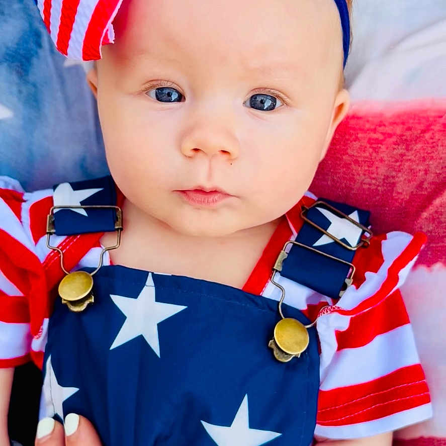 Remi joined the competition — help win amazing prizes! baby, blue, blue_eyes, bow, child, clothing, cute, fabric, face, hand, headband, infant, nails, overalls, pattern, portrait, red, stars, stripes, white
