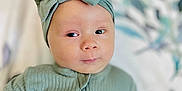 Remi is registered to the contest to win money with this photo: baby, child, infant, face, headband, bow, green_clothing, ribbed_outfit, lying_down, blanket, pattern, soft_focus, portrait, cute, expression, skin, hand, indoors, young, person