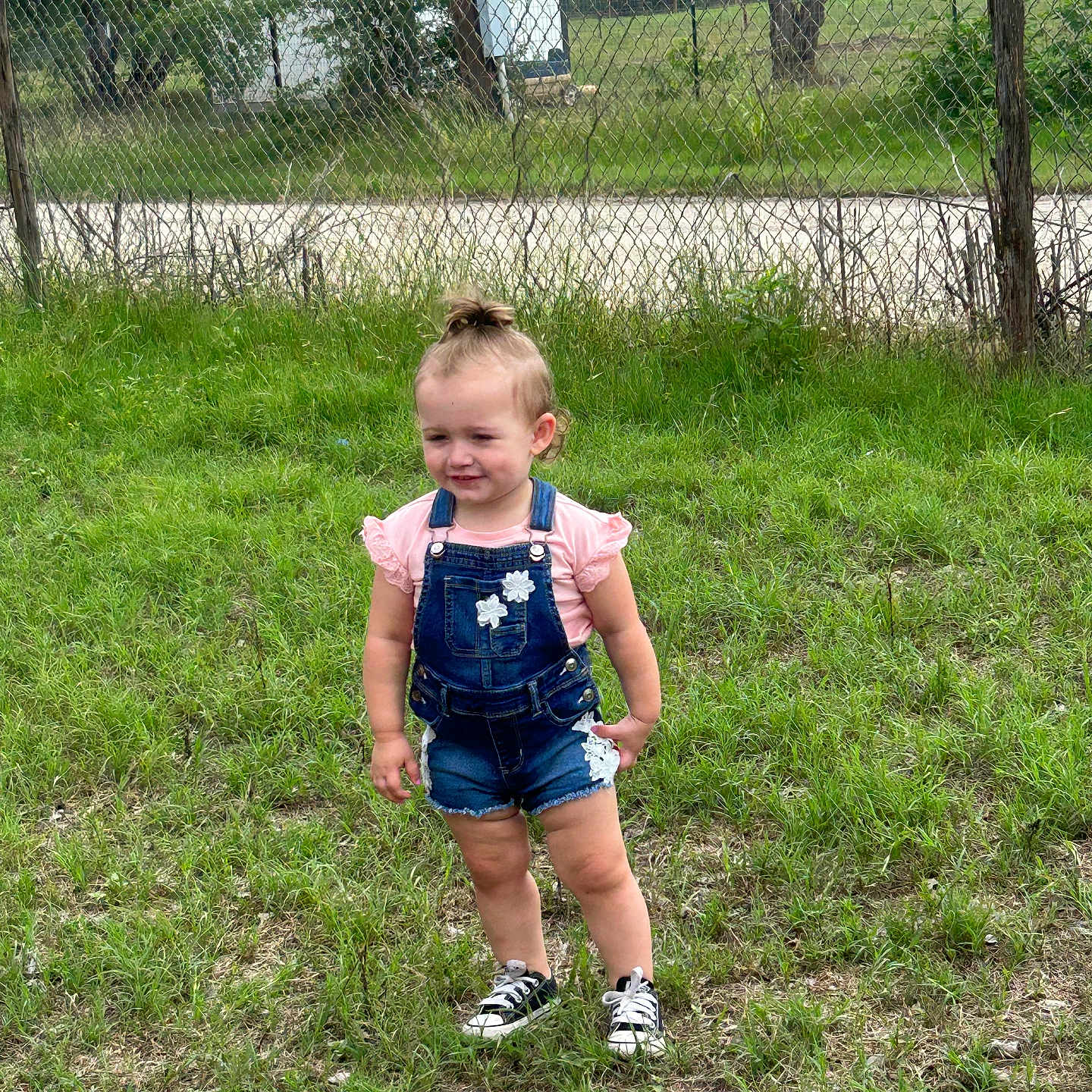 Arington joined the competition — help win amazing prizes! child, toddler, grass, outdoor, fence, denim_overalls, pink_shirt, shorts, sneakers, top_knot, trees, nature, person, summer, daylight, greenery, casual_clothing, standing, cute, young_child
