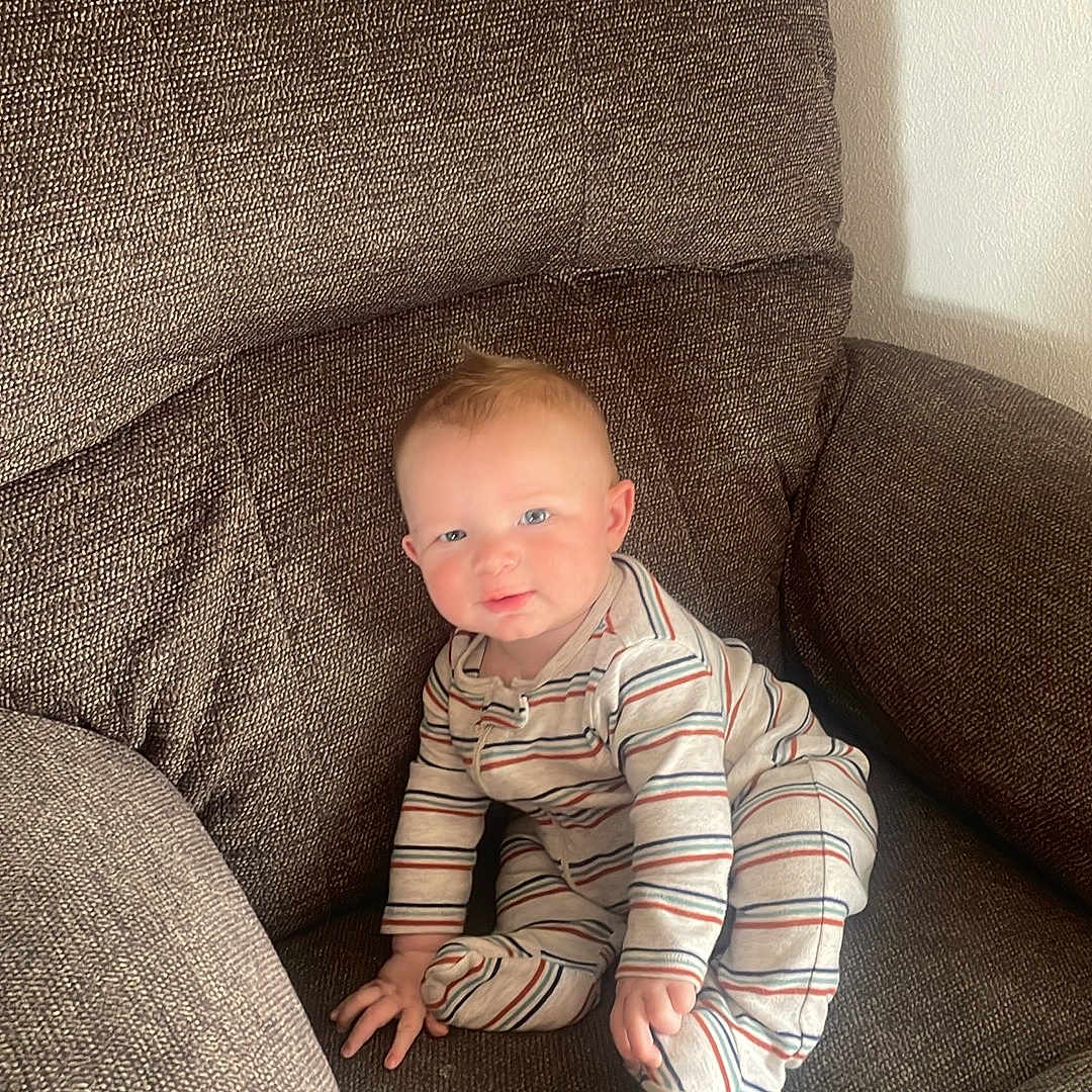 Noah joined the competition — help win amazing prizes! armchair, baby, brown_fabric, child, comfortable, cozy, cushion, cute, furniture, home, indoor, infant, person, portrait, relaxed, sitting, smiling, soft_lighting, striped_pajamas, young_child