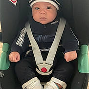Jassim participe au concours pour gagner de l'argent avec cette photo : baby, car_seat, child, seat_belt, clothing, hat, socks, floor, indoor, person, face, hands, footwear, sitting, black_clothing, white_socks, tile_floor, safety, infant, hoodie
