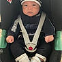 baby, car_seat, child, seat_belt, clothing, hat, socks, floor, indoor, person, face, hands, footwear, sitting, black_clothing, white_socks, tile_floor, safety, infant, hoodie
