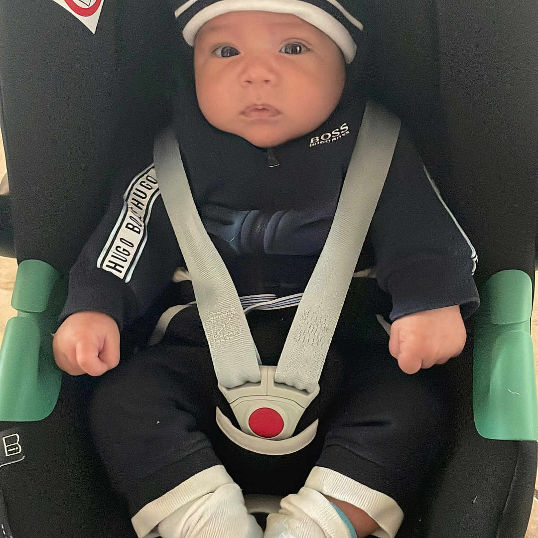 Jassim participe au concours pour gagner de l'argent avec cette photo : baby, black_clothing, car_seat, child, clothing, face, floor, footwear, hands, hat, hoodie, indoor, infant, person, safety, seat_belt, sitting, socks, tile_floor, white_socks