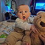 baby, teddy_bear, bed, blanket, striped_pants, toy, room, mirror, painting, television, furniture, person, child, clothing, hand, foot, expression, indoor, soft_toy, surprise