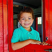Mayson joined the competition — help win amazing prizes! boy, bright_colors, casual_clothing, child, curly_hair, door, face, hand, happy, indoors, natural_light, playful, portrait, red_door, rustic, smiling, turquoise_shirt, window, wood, young