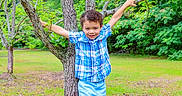 Mayson is registered to the contest to win money with this photo: boy, branches, casual_clothing, child, curly_hair, daylight, grass, greenery, happy, nature, outdoor, park, person, plaid_shirt, playful, shorts, smile, summer, tree, young