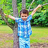 Mayson is registered to the contest to win money with this photo: child, boy, tree, nature, greenery, outdoor, smile, plaid_shirt, shorts, grass, branches, park, happy, playful, person, summer, daylight, curly_hair, casual_clothing, young
