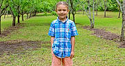Memphis is registered to the contest to win money with this photo: child, boy, smile, standing, outdoor, orchard, trees, grass, greenery, nature, casual_clothing, plaid_shirt, shorts, happy, portrait, daylight, person, young, cute, summer