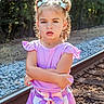 Miyah joined the competition — help win amazing prizes! child, girl, curly_hair, bows, purple_shirt, striped_shorts, railroad_track, gravel, trees, outdoor, sunlight, serious_expression, standing, arms_crossed, nature, summer_clothing, person, portrait, young_child, fashion