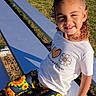 Miyah is registered to the contest to win money with this photo: child, curly_hair, pony_tail, white_tshirt, sunflower_pants, outdoor, grass, bleachers, smiling, sitting, sunlight, happy, casual_clothing, young_girl, daytime, nature, patterned_pants, colorful, portrait, playful