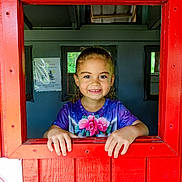 Miyah joined the competition — help win amazing prizes! bright_colors, casual_clothing, child, colorful_shirt, curly_hair, cute, face, hands, happy, indoor, natural_light, person, playhouse, portrait, red_frame, roses, smiling, window, wooden, young