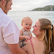Matteo is registered to the contest to win money with this photo: baby, child, parents, family, smiling, happy, portrait, outdoor, seaside, beach, ocean, water, coastline, hillside, island, man, woman, holding, tattoo, summer