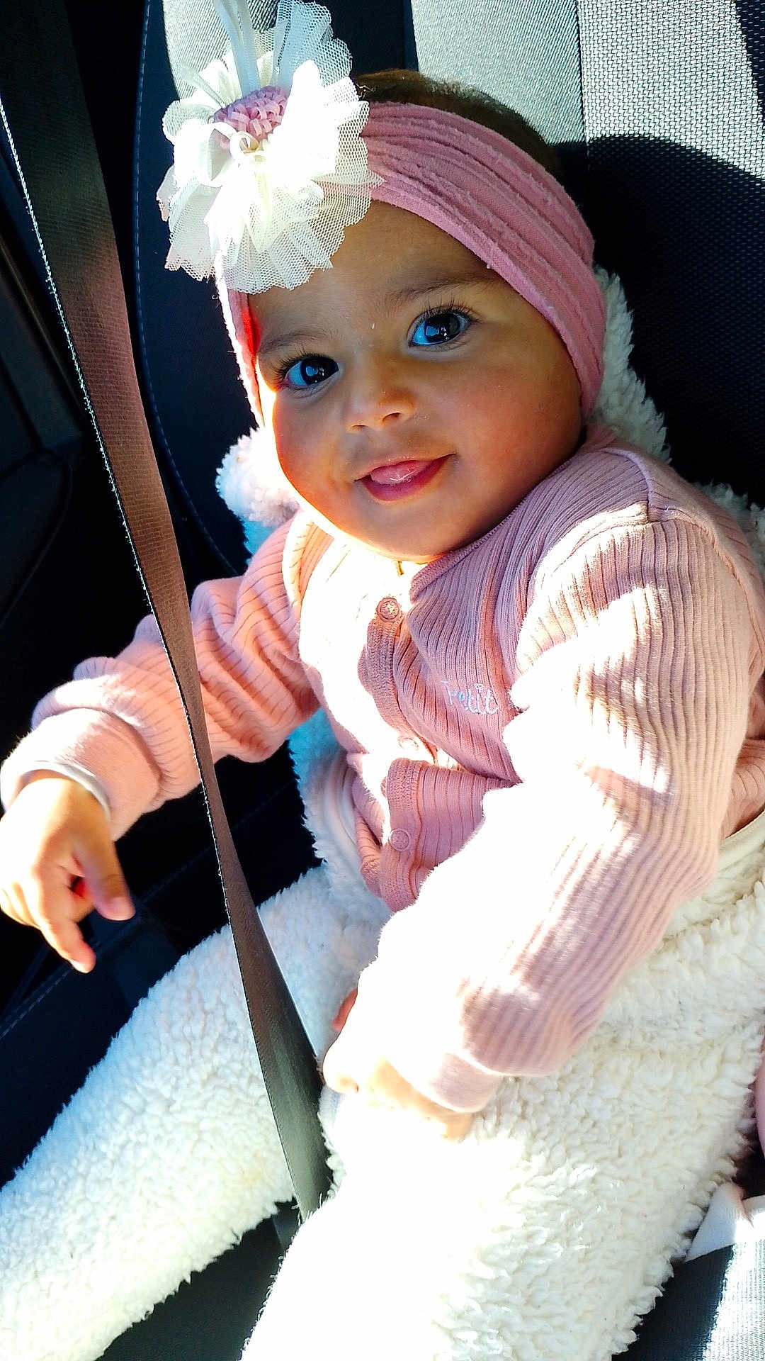 Ayana a rejoint le concours — aidez-le/la à gagner de superbes lots ! baby, child, headband, flower, pink_clothing, sweater, white_pants, car_seat, seatbelt, smiling, tongue_out, sunlight, cozy, cute, portrait, indoor, happy, infant, safe, closeup