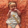 baby, infant, smile, pacifier, blanket, hair_bow, onesie, textured_background, cute, happy, portrait, lying_down, hands, skin, eyes, chubby_cheeks, peach_pattern, pacifier_clip, coral_blanket, cozy