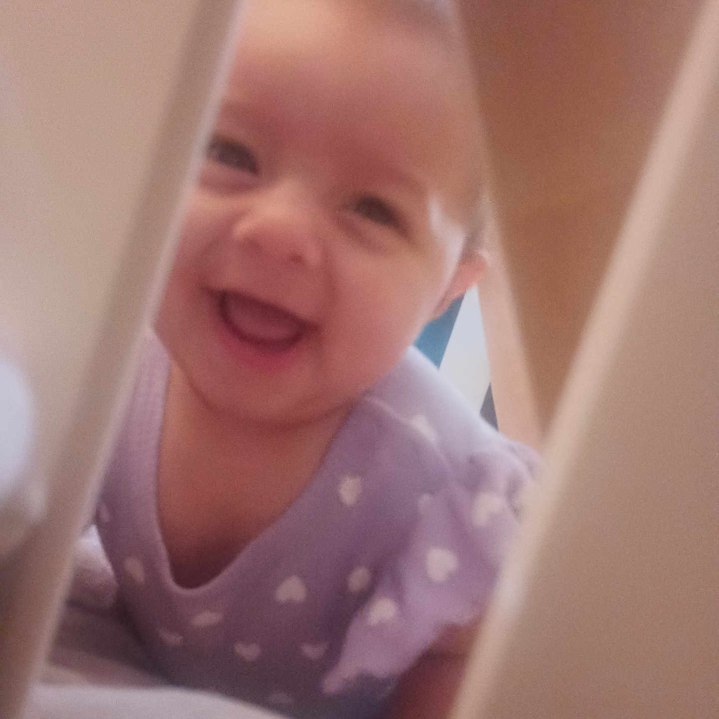 Aitana is registered to the contest to win money with this photo: baby, smiling, infant, purple_clothing, heart_pattern, face, closeup, happy, cute, child, crawling, indoors, cradle, bars, person, young, soft_lighting, expression, joyful, playful