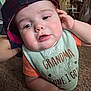 baby, child, face, headwear, cap, bib, orange_shirt, hand, indoor, carpet, closeup, cute, curious, infant, person, portrait, soft_lighting, chubby_cheeks, expression, casual