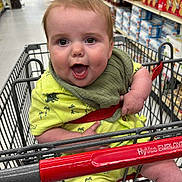 James joined the competition — help win amazing prizes! baby, child, shopping_cart, grocery_store, yellow_outfit, bib, smiling, happy, infant, retail, aisle, products, dinosaur_print, person, cute, indoor, cart_handle, clothing, footwear, socks