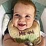 James joined the competition — help win amazing prizes! baby, smiling, bib, infant, child, cute, happy, face, portrait, chubby_cheeks, seated, indoors, soft_toy, cushion, clothing, skin, hands, closeup, young_child, person