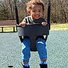 toddler, child, swing, playground, outdoor, smiling, happy, curly_hair, blue_jeans, black_shoes, black_swing, grass, bench, trees, sunny, daytime, person, park, casual_clothing, play