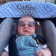 Caëlan a rejoint le concours — aidez-le/la à gagner de superbes lots ! baby, child, car_seat, sunglasses, overalls, white_shirt, plush_headrest, straps, hand, face, brick_wall, outdoor, comfort, cute, infant, portrait, casual, fashion, seatbelt, blue
