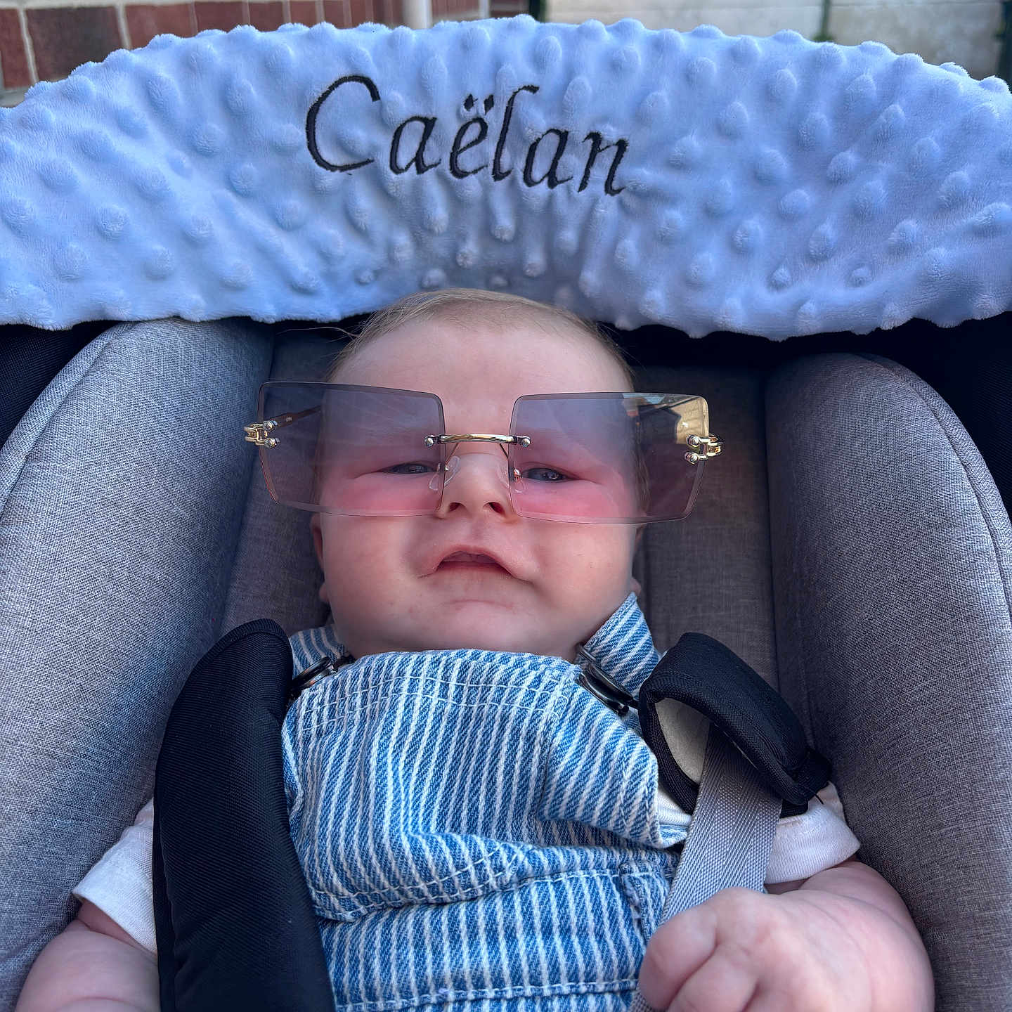 Caëlan a rejoint le concours — aidez-le/la à gagner de superbes lots ! baby, blue, brick_wall, car_seat, casual, child, comfort, cute, face, fashion, hand, infant, outdoor, overalls, plush_headrest, portrait, seatbelt, straps, sunglasses, white_shirt