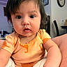 Payton is registered to the contest to win money with this photo: baby, infant, child, onesie, orange_clothing, dinosaur_print, face, eyes, mouth, indoor, living_room, clock, picture_frame, curious, cute, person, skin, hair, hand, portrait
