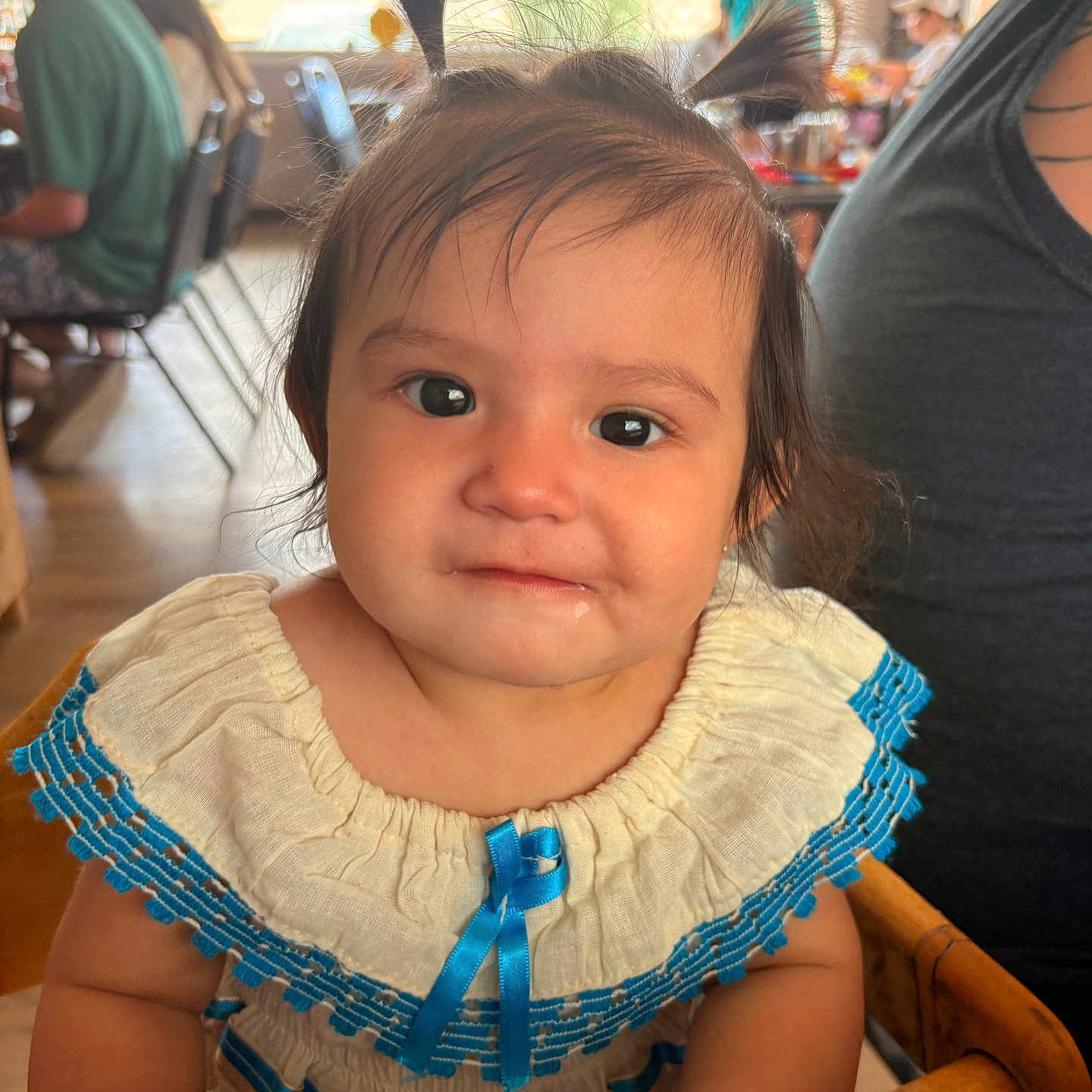 Payton is registered to the contest to win money with this photo: toddler, child, pigtails, dress, blue, white, high_chair, indoor, people, background, face, curious, hair, cute, person, smile, natural_light, wood, seated, baby