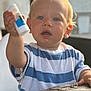 Alezio a rejoint le concours — aidez-le/la à gagner de superbes lots ! child, toddler, blue_eyes, blonde_hair, striped_shirt, white_and_blue, sitting, table, wooden_table, indoor, curious, holding_object, small_bottle, face, portrait, person, casual_clothing, young_child, expression, closeup