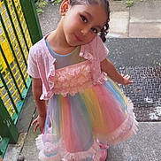 Alaia joined the competition — help win amazing prizes! child, girl, dress, pink_shoes, rainbow_colors, bow, hair, pose, outdoor, fence, gate, bicycle, concrete, playful, smile, earrings, pastel, cute, toddler, fashion