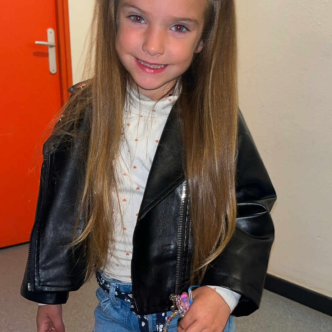Inaya participe au concours pour gagner de l'argent avec cette photo : bracelets, casual, child, clothing, door, fashion, floor, girl, hair_clips, happy, indoor, jeans, leather_jacket, long_hair, orange, person, portrait, smiling, standing, wall