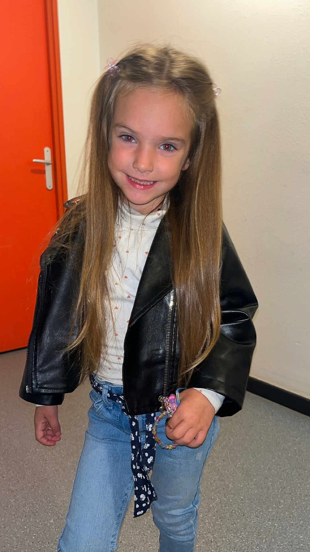 Inaya participe au concours pour gagner de l'argent avec cette photo : child, girl, smiling, long_hair, leather_jacket, jeans, bracelets, indoor, door, orange, wall, floor, hair_clips, standing, fashion, casual, happy, person, portrait, clothing