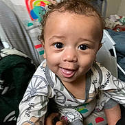 Weston joined the competition — help win amazing prizes! toddler, child, baby, smiling, face, pajamas, curly_hair, indoors, hand, playful, expression, person, closeup, cute, happy, seated, colorful, background, cozy, young_child