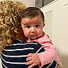 adult, baby, cabinets, child, close_up, curiosity, curly_hair, embrace, expression, face, hand, holding, home, indoor, person, pink_clothing, portrait, skin, striped_shirt, toddler